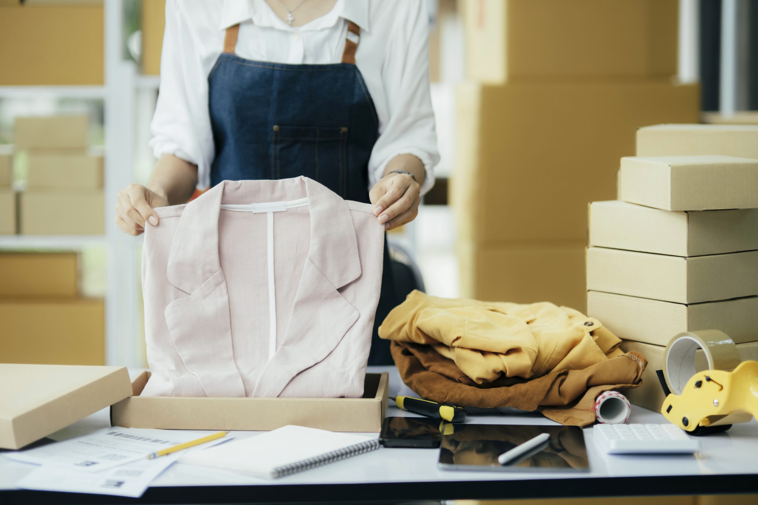 Small business owner packing clothes in the box at workplace.